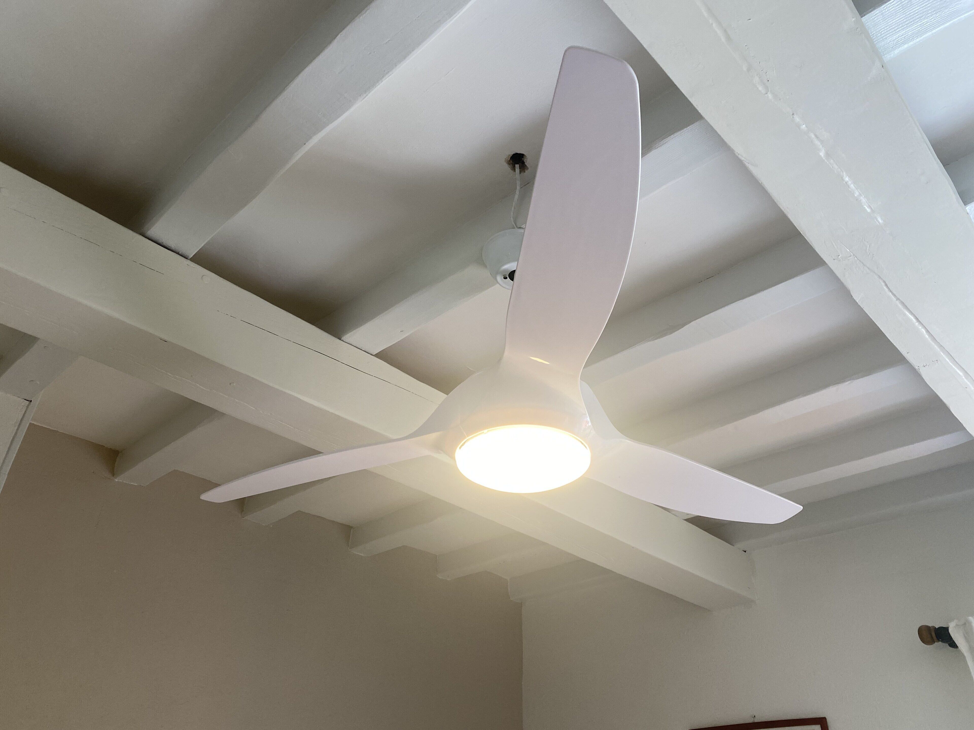 Um ventilador de teto com luminária em um quarto com paredes brancas e vigas aparentes.