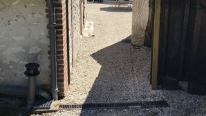 En smal passage med grusgulv, murstensvægge og et metalgitter.