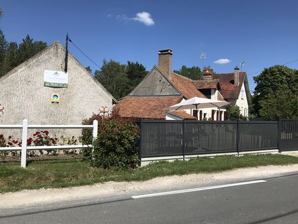 A building with a stone facade, a sign with a phone number, and a fenced area with a white fence and red flowers.