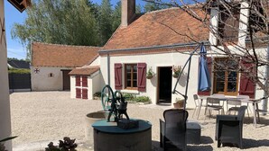 En rustik bygning med en grusgård, udendørs siddepladser og en vandpumpe.
