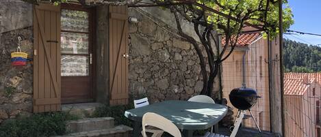 A stone wall with a wooden door, a table with chairs, and a grill outside.