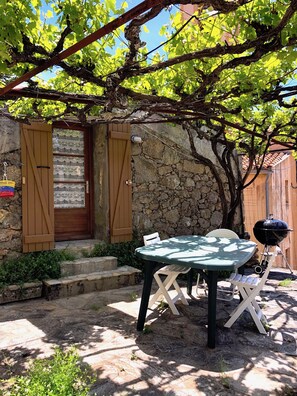 A rustic outdoor seating area with a table and chairs, a wooden door, and a stone wall. - pretty stone house in the heart of the village (Évisa)