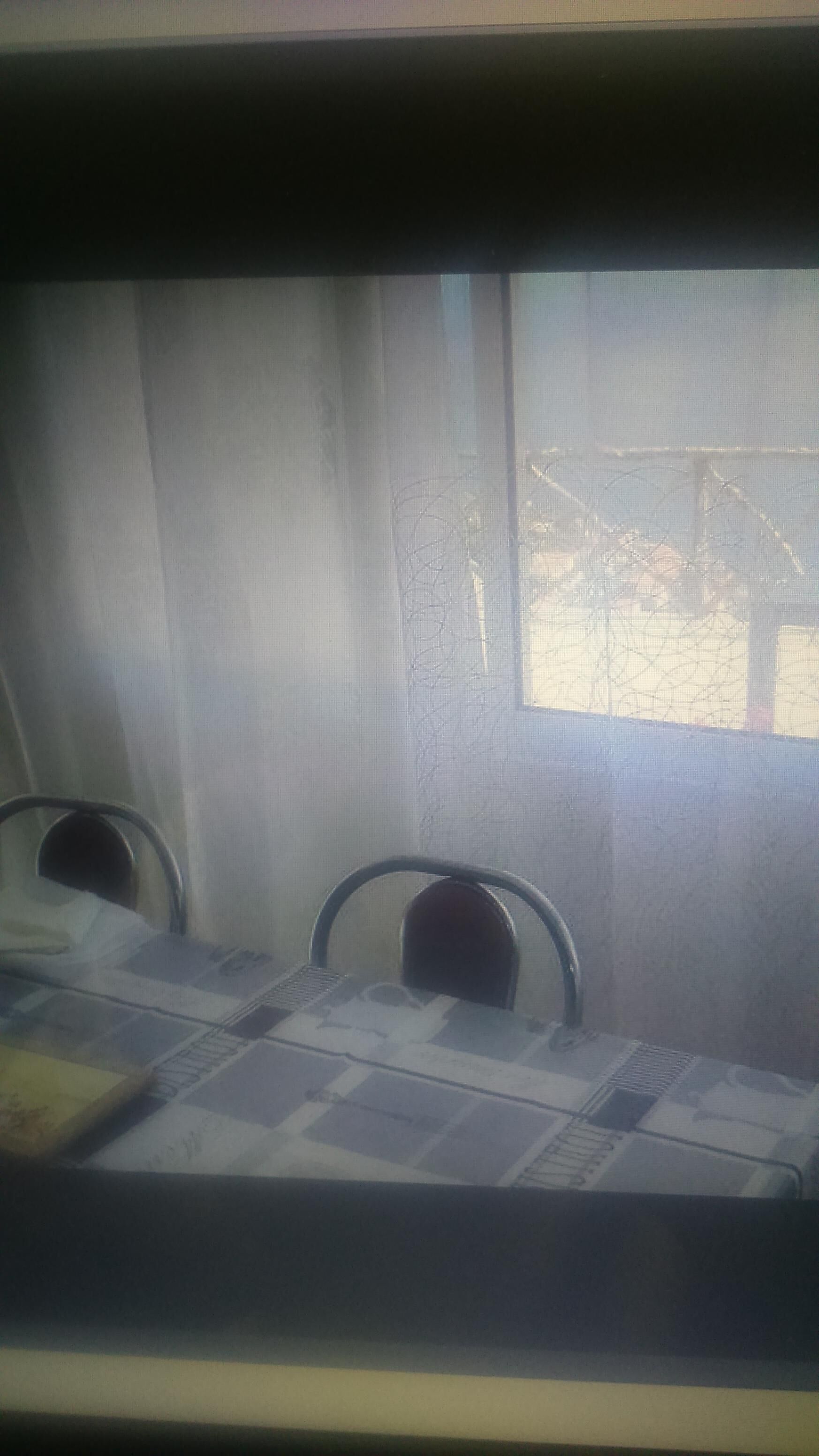 A room with a table and chairs, a window with a view of a fenced area, and curtains.