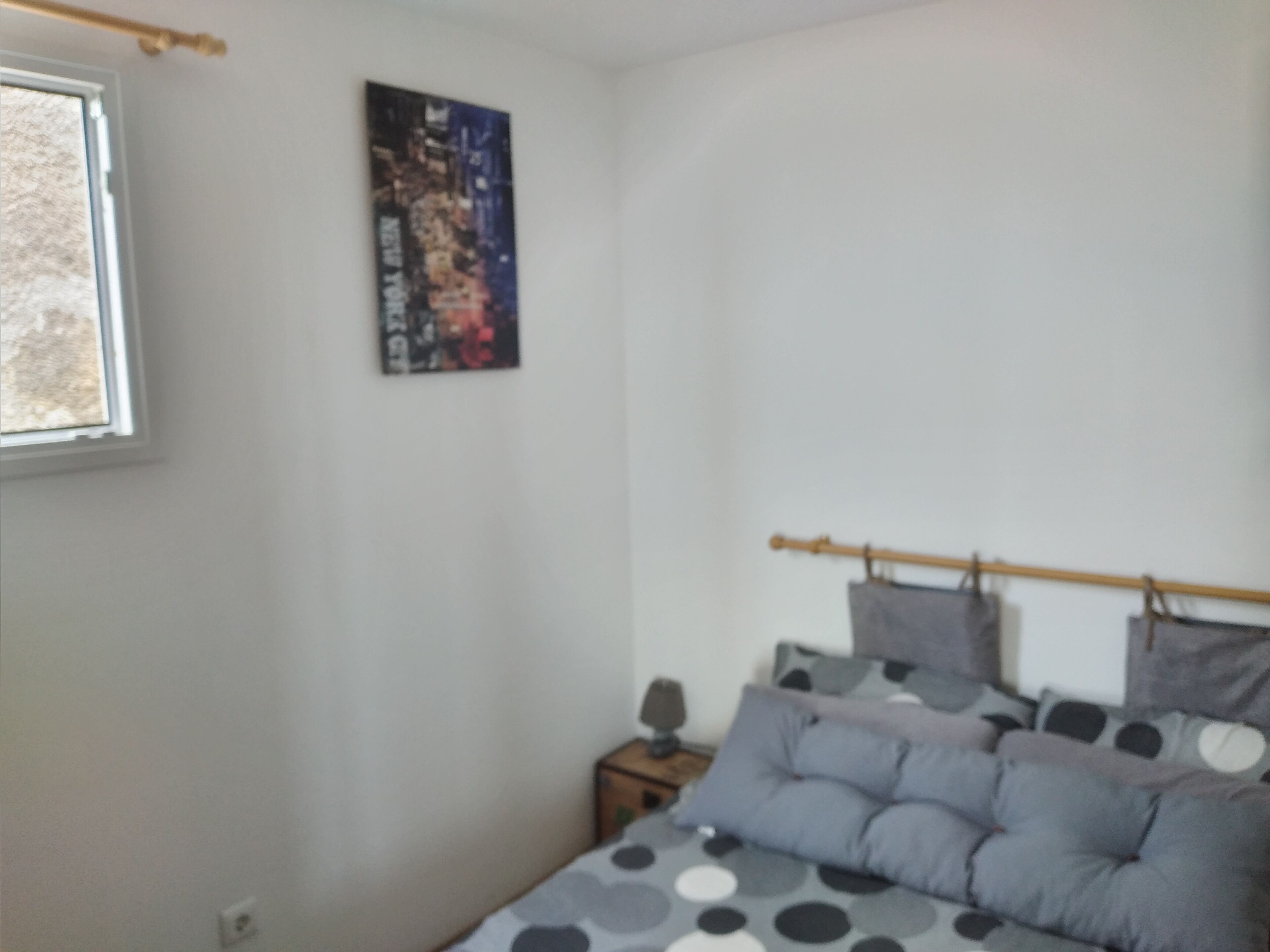 A bedroom with a bed, pillows, a nightstand, a poster on the wall, and a window.