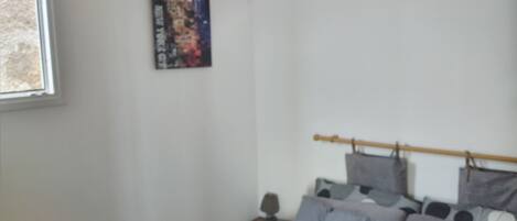 A bedroom with a bed, pillows, a nightstand, a poster on the wall, and a window.