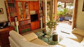 A living room with a sofa, a coffee table, a bookshelf, and a television. - AIR-CONDITIONED, SINGLE-STOREY VILLA, SEA AND CORSICAN VIEWS LARGE GARDEN, DOGS ALLOWED (Villeneuve-Loubet)
