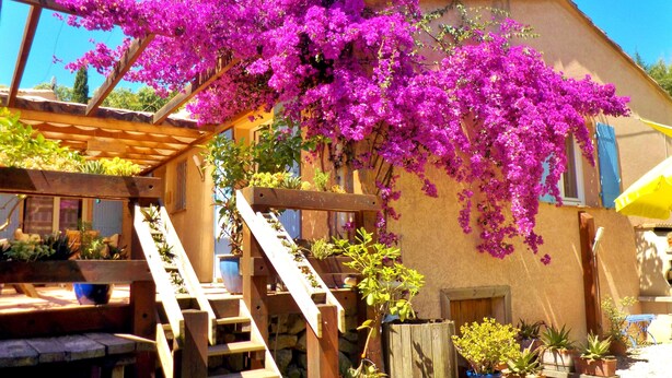 A wooden deck with a wooden staircase leading to a covered area, surrounded by potted plants and a building with a stucco exterior. - AIR-CONDITIONED, SINGLE-STOREY VILLA, SEA AND CORSICAN VIEWS LARGE GARDEN, DOGS ALLOWED (Villeneuve-Loubet)