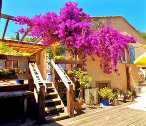 A wooden deck with a wooden staircase leading to a covered area, surrounded by potted plants and a building with a stucco exterior. - AIR-CONDITIONED, SINGLE-STOREY VILLA, SEA AND CORSICAN VIEWS LARGE GARDEN, DOGS ALLOWED (Villeneuve-Loubet)