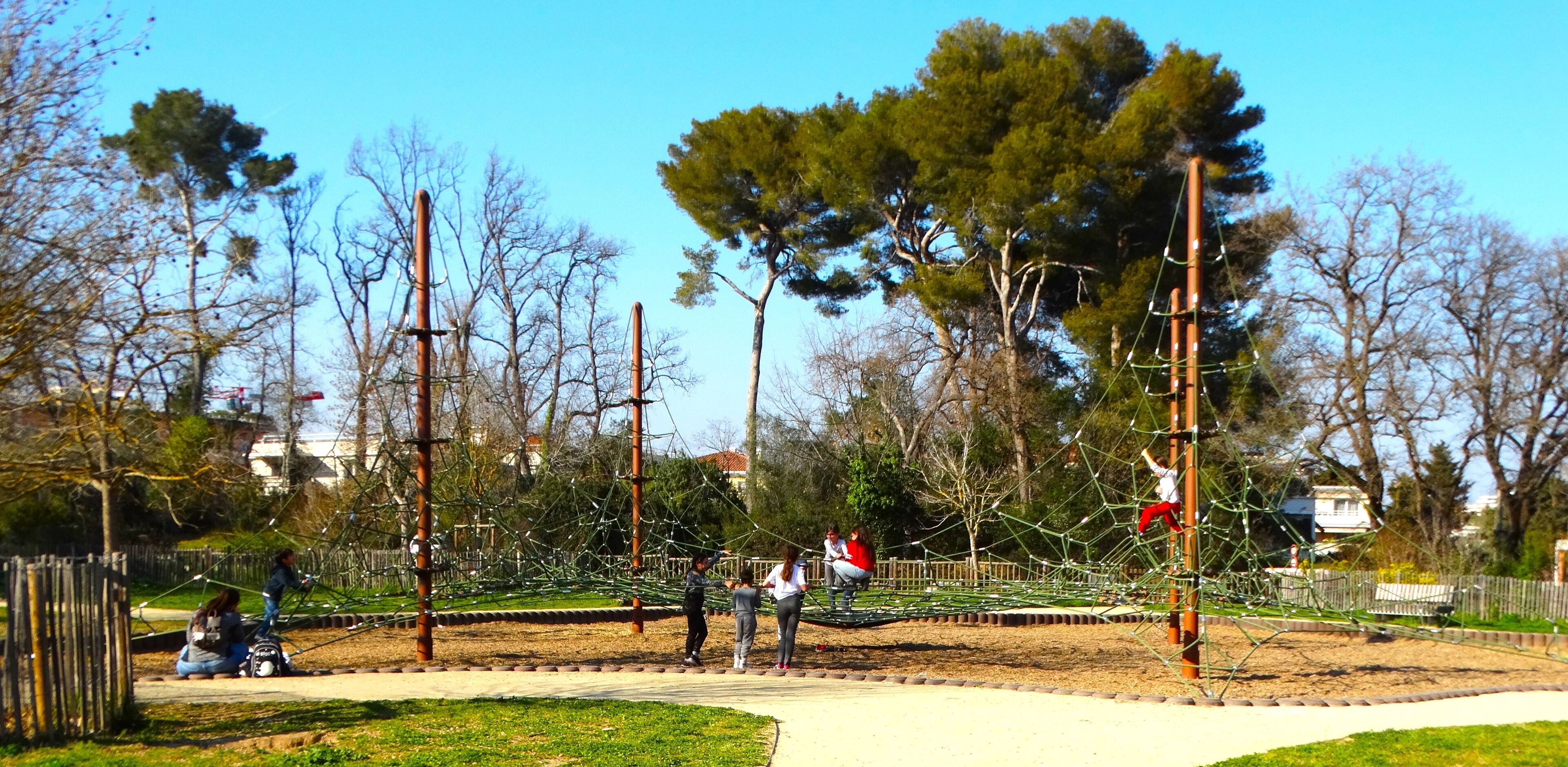 A playground with swings and climbing structures surrounded by trees and a fence.