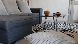 Una sala moderna con un sofá grisáceo, cojines estampados, una mesita baja con adornos y una alfombra con diseño.