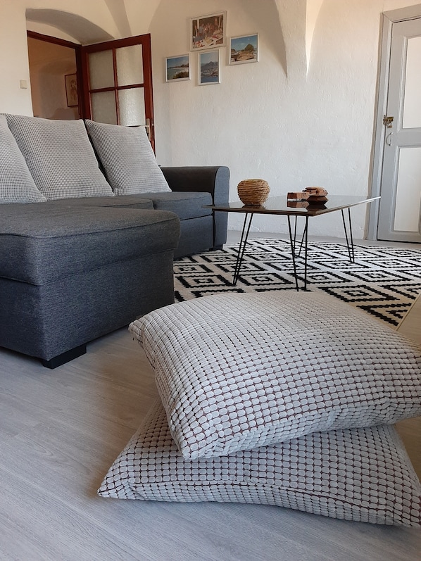 A modern living room with a grey sofa, patterned cushions, a small table with decorative items, and a patterned rug.