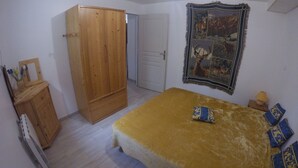 Een slaapkamer met een bed, een houten kledingkast, een deur en een wandtapijt.