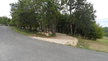 Ein asphaltierter Weg schlängelt sich durch ein bewaldetes Gebiet, begleitet von einem Schotterweg und Felsen.
