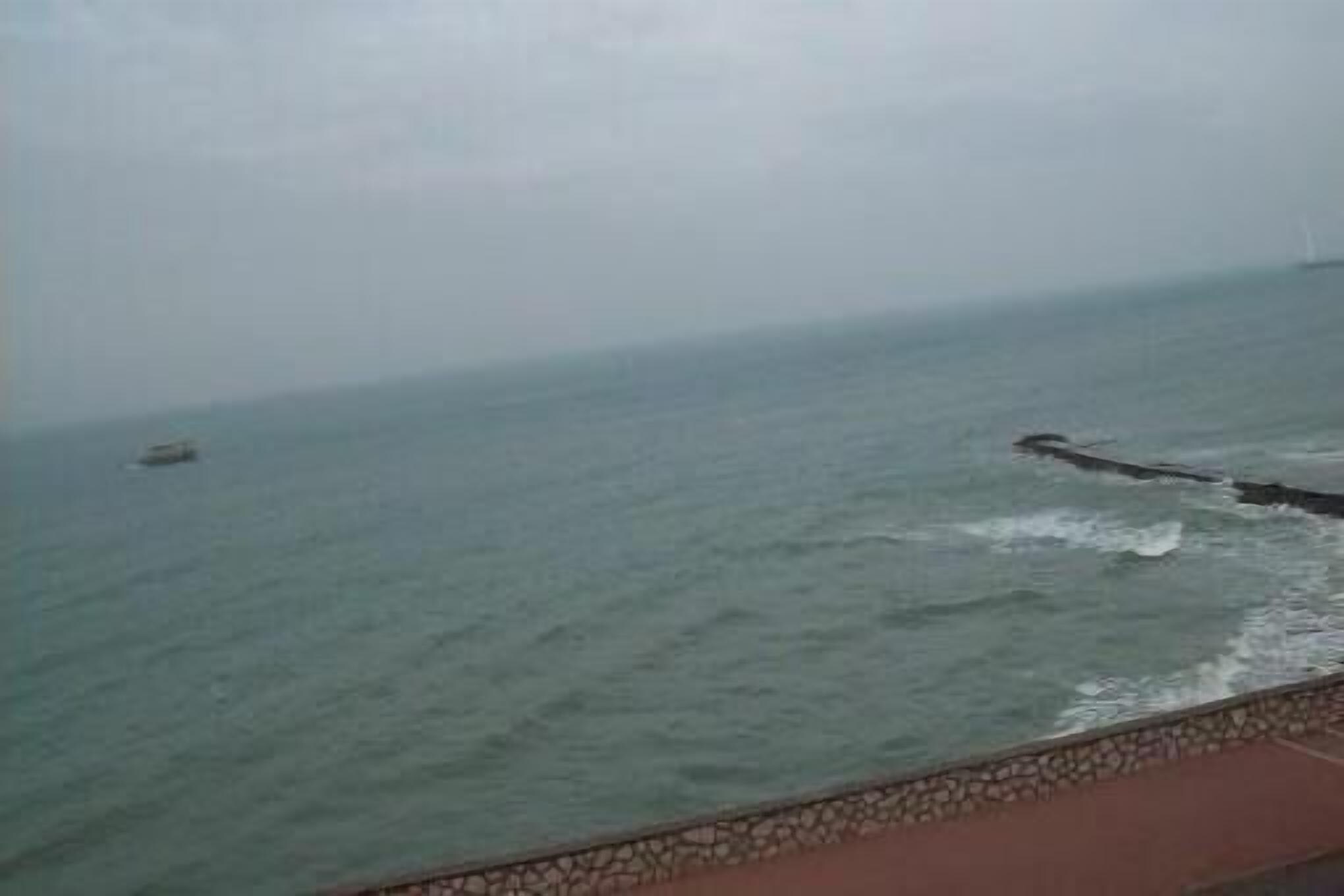 A coastal view with a stone wall and a boat in the distance.