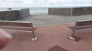Un chemin pavé bordé de bancs, un mur de pierre et une vue sur la mer.
