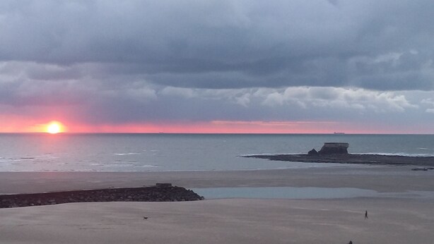 Une plage au coucher du soleil, avec des rochers et une mer calme.