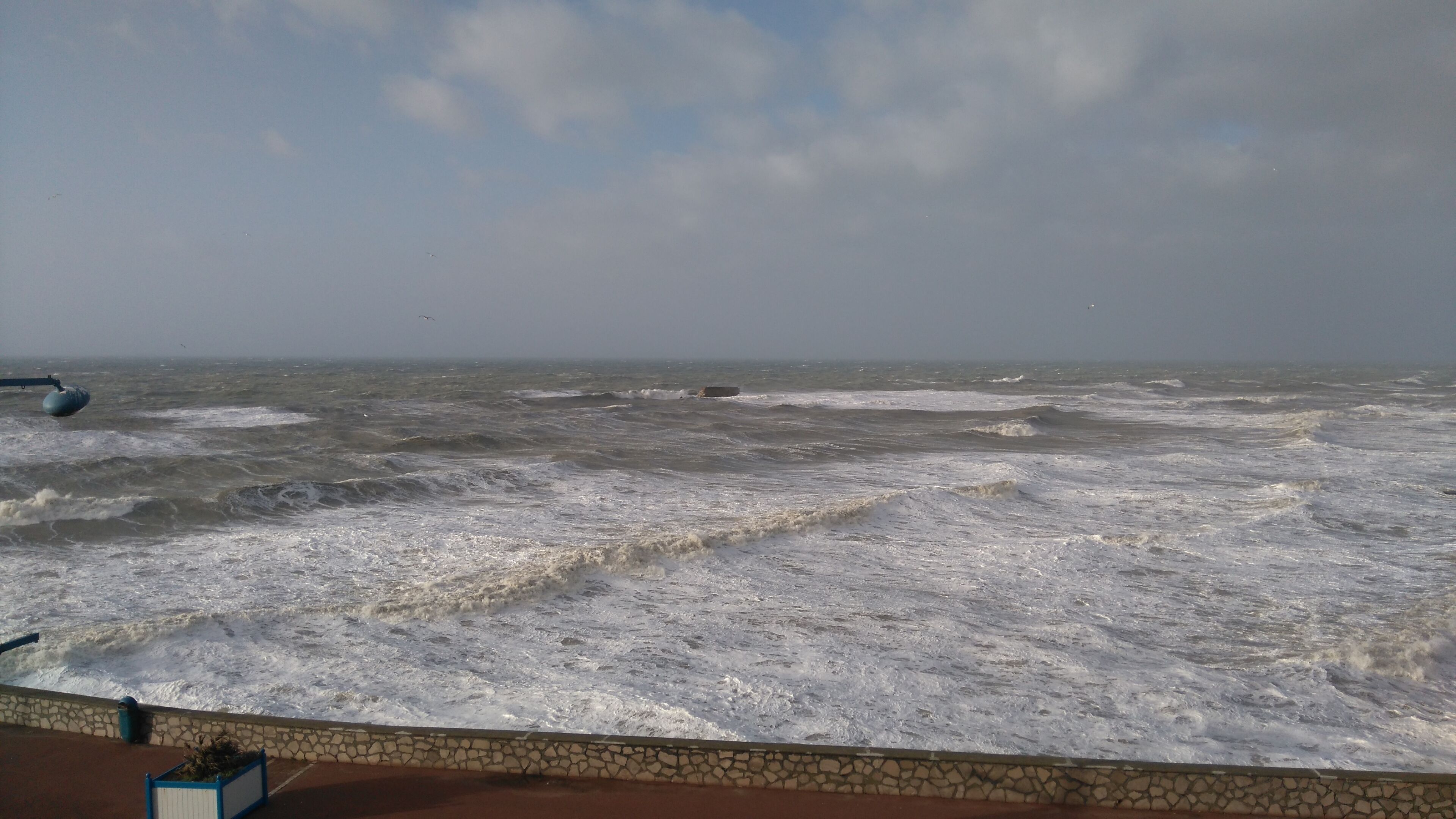 Blick auf das Meer mit brechenden Wellen, die auf eine gepflasterte Fläche treffen.