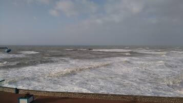 Blick auf das Meer mit brechenden Wellen, die auf eine gepflasterte Fläche treffen.