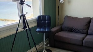 Une pièce comprenant un télescope monté sur un trépied, une chaise bleue, un canapé marron et un lampadaire.