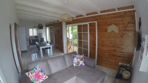 A spacious living area with a grey sofa, a dining table, and a kitchen in the background. - Villa Marga: pretty new Creole villa (Capesterre - Belle - Eau)