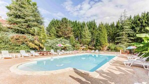 Une piscine rectangulaire dont les bords sont recouverts de petits galets, entourée de chaises longues et de parasols.