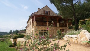 Une maison en pierre avec un balcon en bois et un jardin à l’avant.
