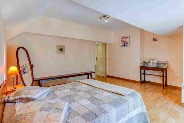 Une chambre à coucher comprenant un lit, une table de chevet, un miroir et une porte donnant sur une autre pièce.