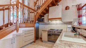 Une cuisine avec un escalier en bois, une cuisinière, un four à micro-ondes et un dosseret carrelé.