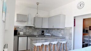 Eine kompakte Küche mit grauen Schränken, einer gefliesten Rückwand, einer kleinen Kücheninsel mit Barhocker, einer Mikrowelle und einer Kaffeemaschine.