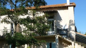 Ein zweistöckiges Gebäude mit Balkon, Schornstein und Garten mit roten Blumen.