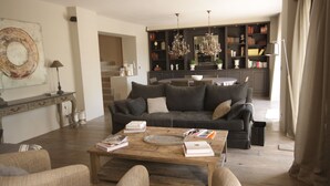 Un salon moderne avec un canapé, une table basse et des livres. On y trouve également un coin repas agrémenté d’un lustre et, en arrière-plan, des étagères à livres.