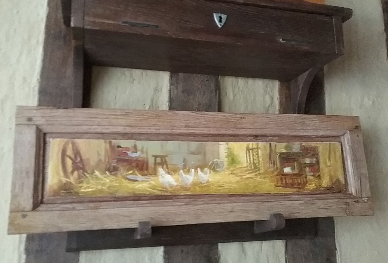 Une étagère rustique en bois, fixée au mur, sur laquelle est posée une image encadrée représentant un paysage rural.