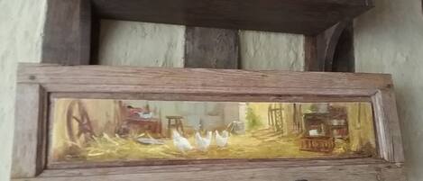Une étagère rustique en bois, fixée au mur, sur laquelle est posée une image encadrée représentant un paysage rural.