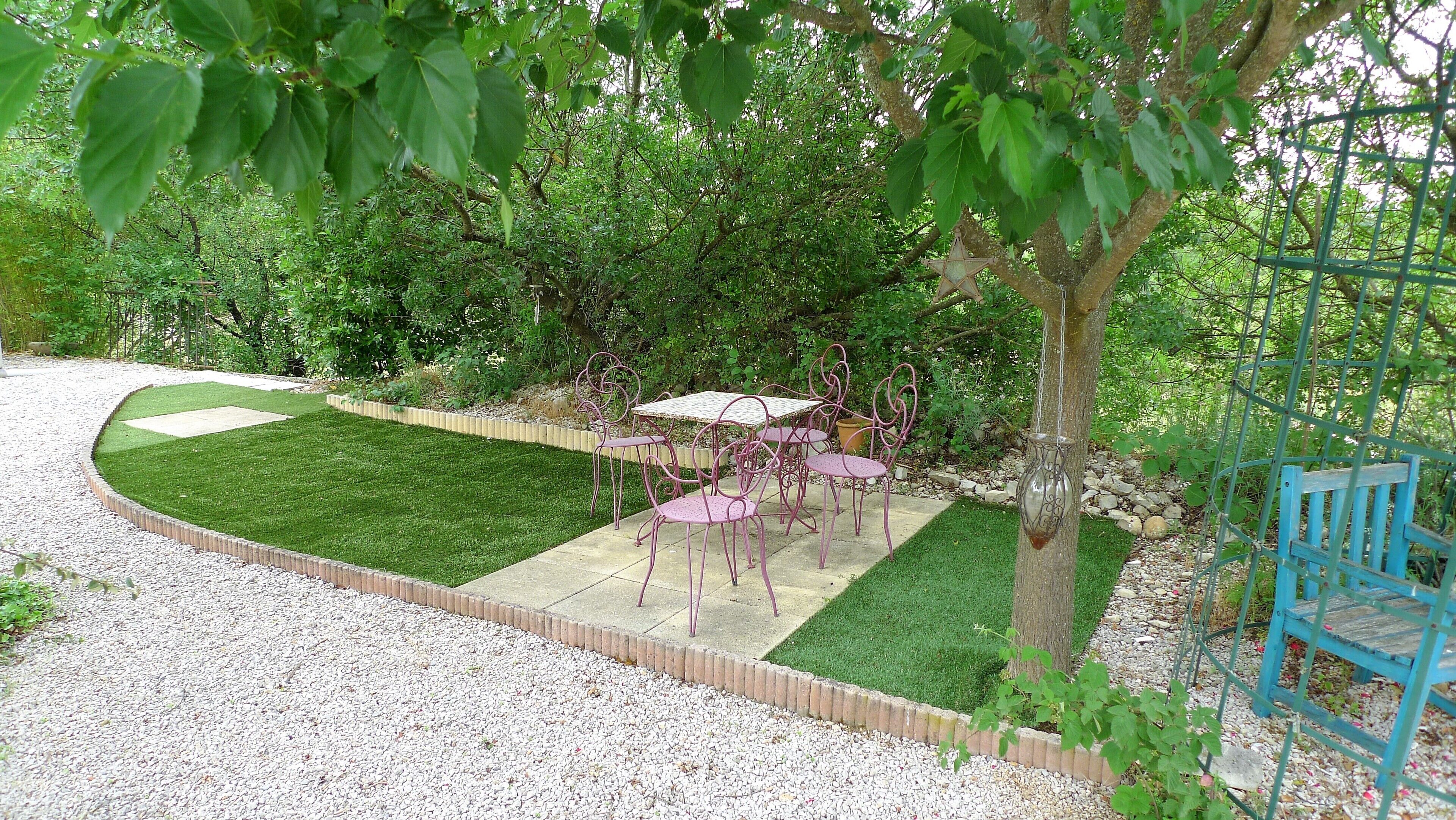 A garden patio with a table and chairs, surrounded by a gravel path and green grass.