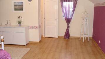 Una habitación con piso de madera, puerta blanca, cortina morada, mueble blanco y una pequeña planta.