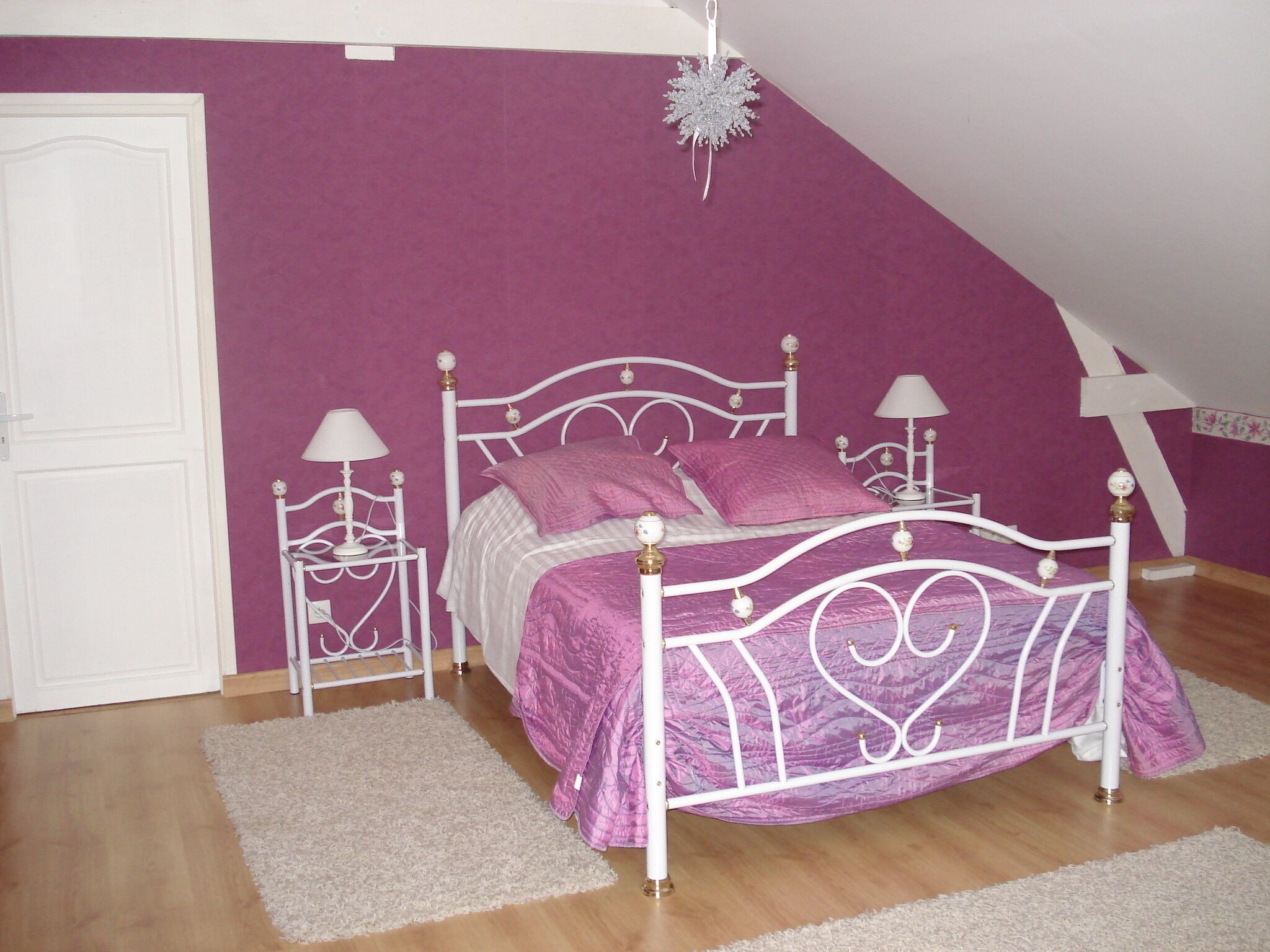 Ein Schlafzimmer mit einem Bettgestell aus weißem Metall, rosa Bettwäsche und einer weißen Tür.