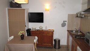 A compact kitchen with a dining table, chairs, a TV, a sink, and a trash can.