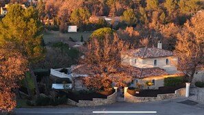 Ein zweigeschossiges Haus mit Ziegeldach, umgeben von Bäumen und einer Steinmauer.