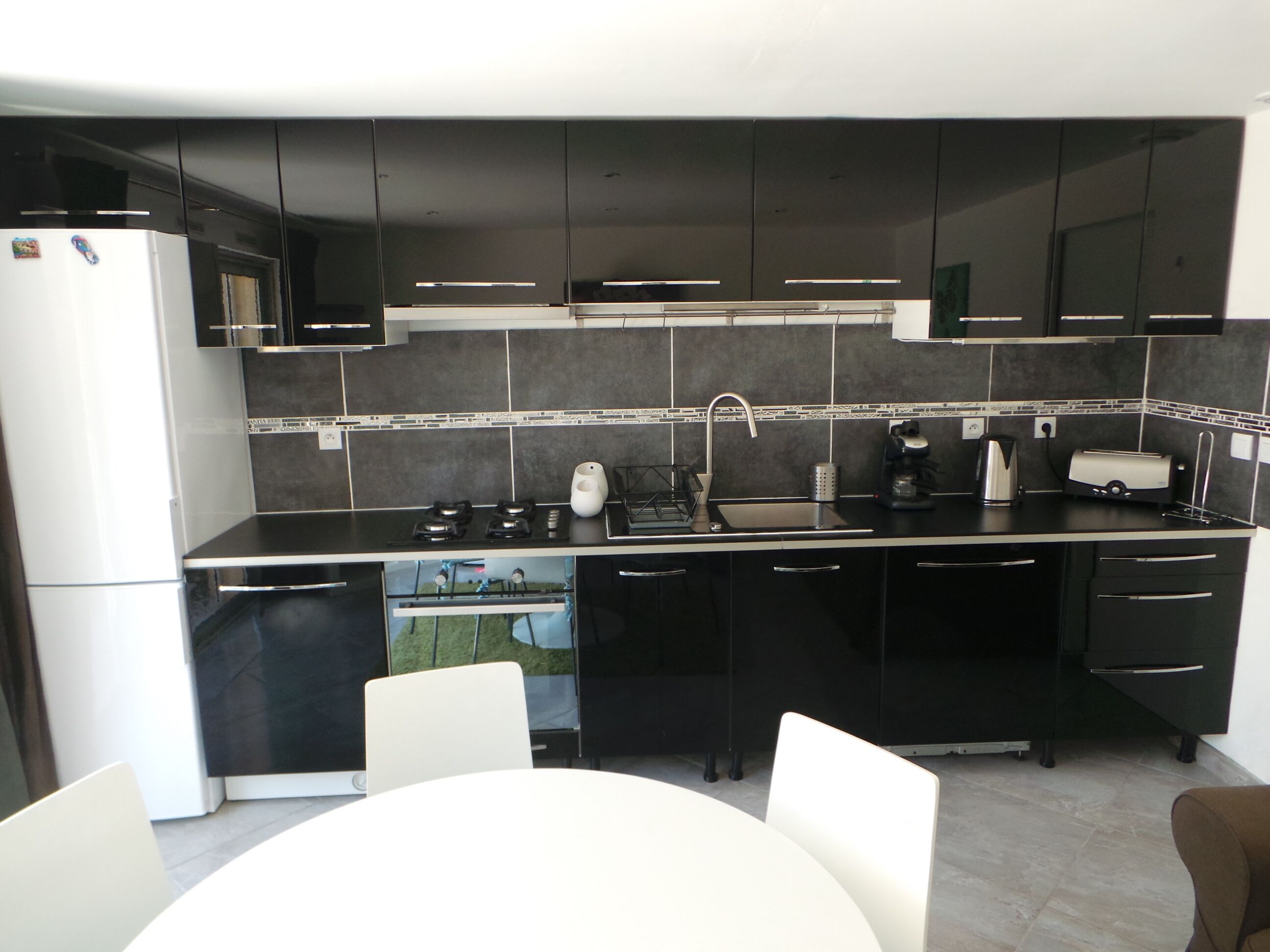 A modern kitchen with black cabinets, a white refrigerator, a gas stove, a sink, and a coffee maker.