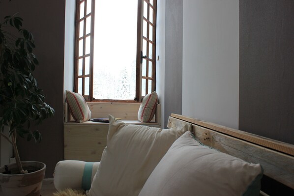 A bedroom with a wooden headboard, a window with wooden shutters, a potted plant, and a bed with white bedding.