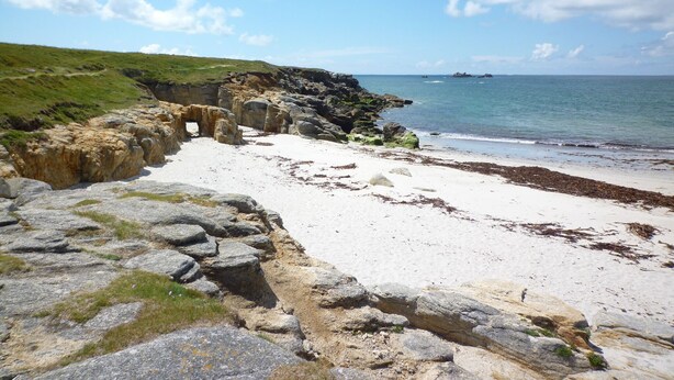 Un paysage côtier caractérisé par des formations rocheuses, une plage de sable et un ciel bleu dégagé.