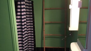A bathroom with a green wall, a white sink, a striped shower curtain, and a wooden ladder. - Apartment for rent in family residence (Le Grau-du-Roi)
