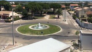 A roundabout with a central fountain, surrounded by residential buildings and greenery. - Apartment for rent in family residence (Le Grau-du-Roi)