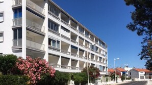 A multi-story hotel with balconies, a clear sky, and a road in the foreground. - Apartment for rent in family residence (Le Grau-du-Roi)