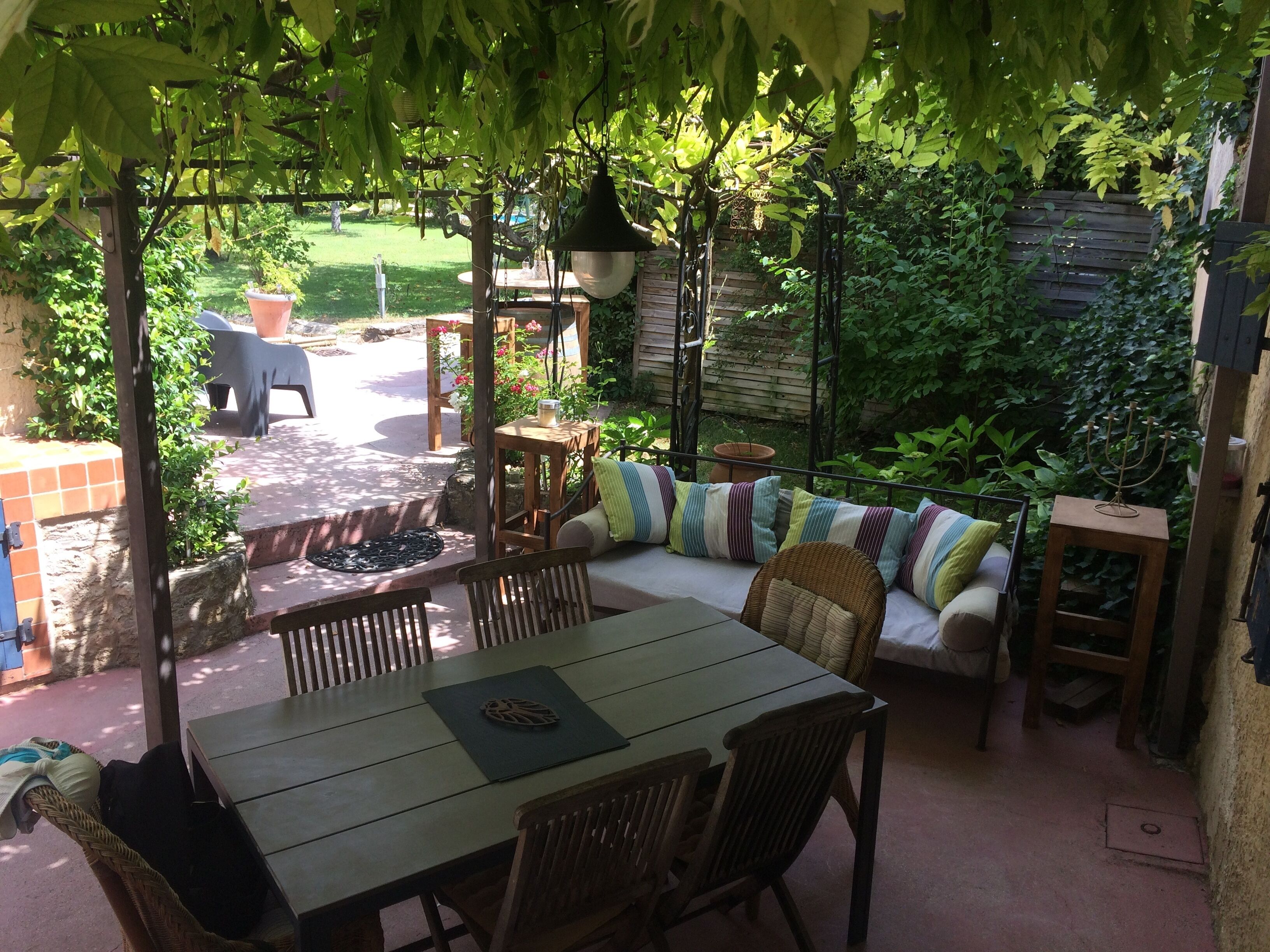Eine Terrasse im Freien mit einem Holztisch und Stühlen, einer gepolsterten Bank und einer hängenden Leuchte.