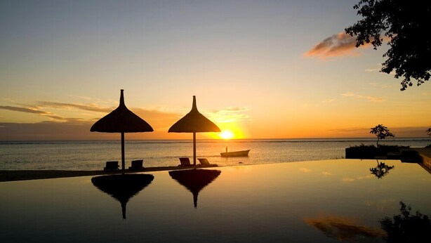 Una piscina infinita con dos sombrillas, un bote y vistas al atardecer.