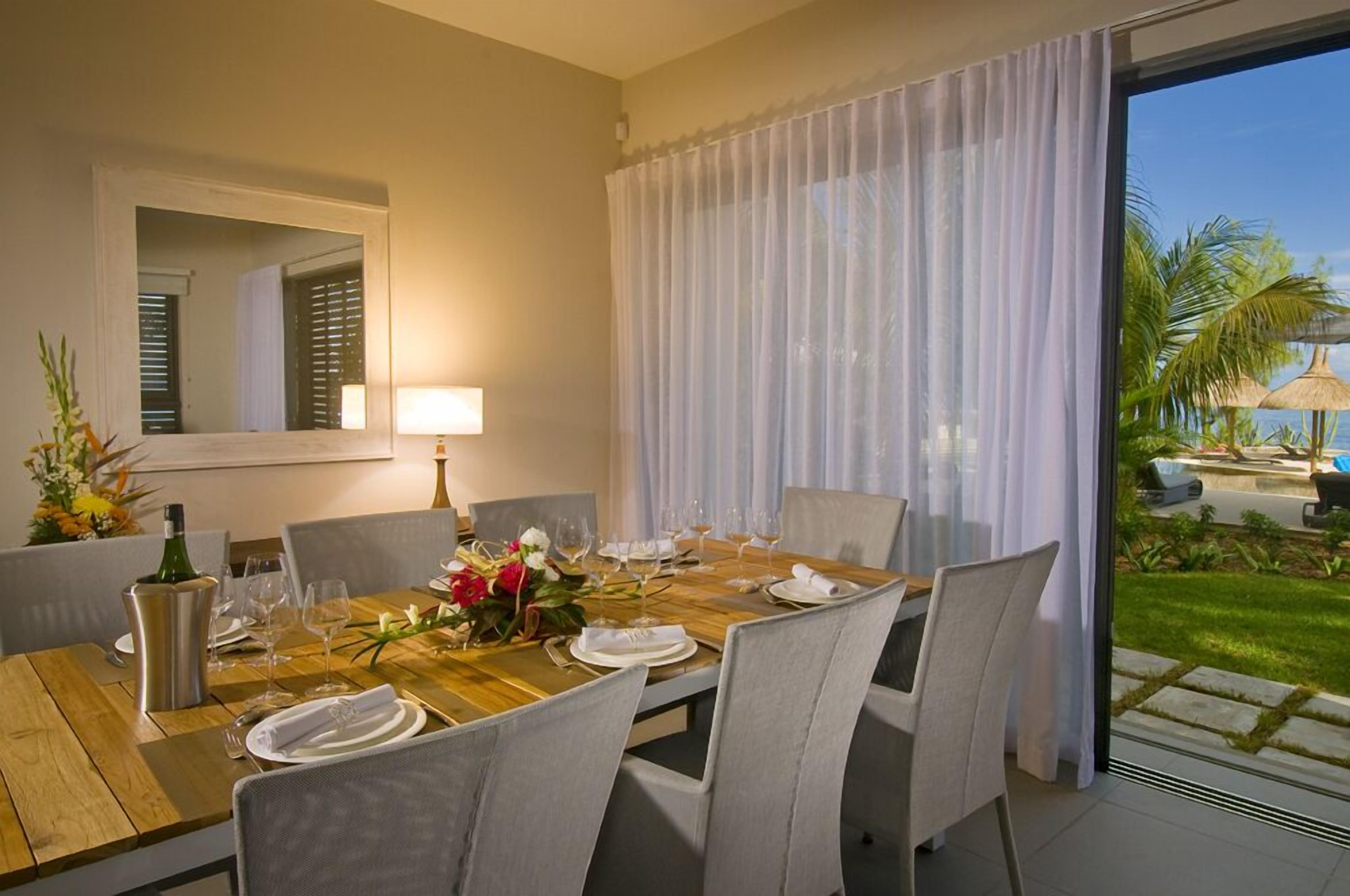 Un coin repas avec une table en bois dressée pour quatre personnes, un vase de fleurs et une bouteille de vin.