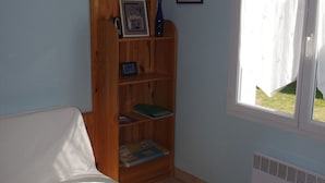 A room with a wooden table, a white sofa, a wooden bookshelf, a hanging lamp, and a window with a curtain. - Terraced house, independent, 100 m from the beach of Rémigeasse (Dolus-D'oléron)