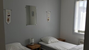 A room with two single beds, a bedside table with a lamp, a mirror, and two wall decorations. - Terraced house, independent, 100 m from the beach of Rémigeasse (Dolus-D'oléron)