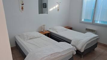 A room with two beds, a window, and a wall-mounted light fixture.